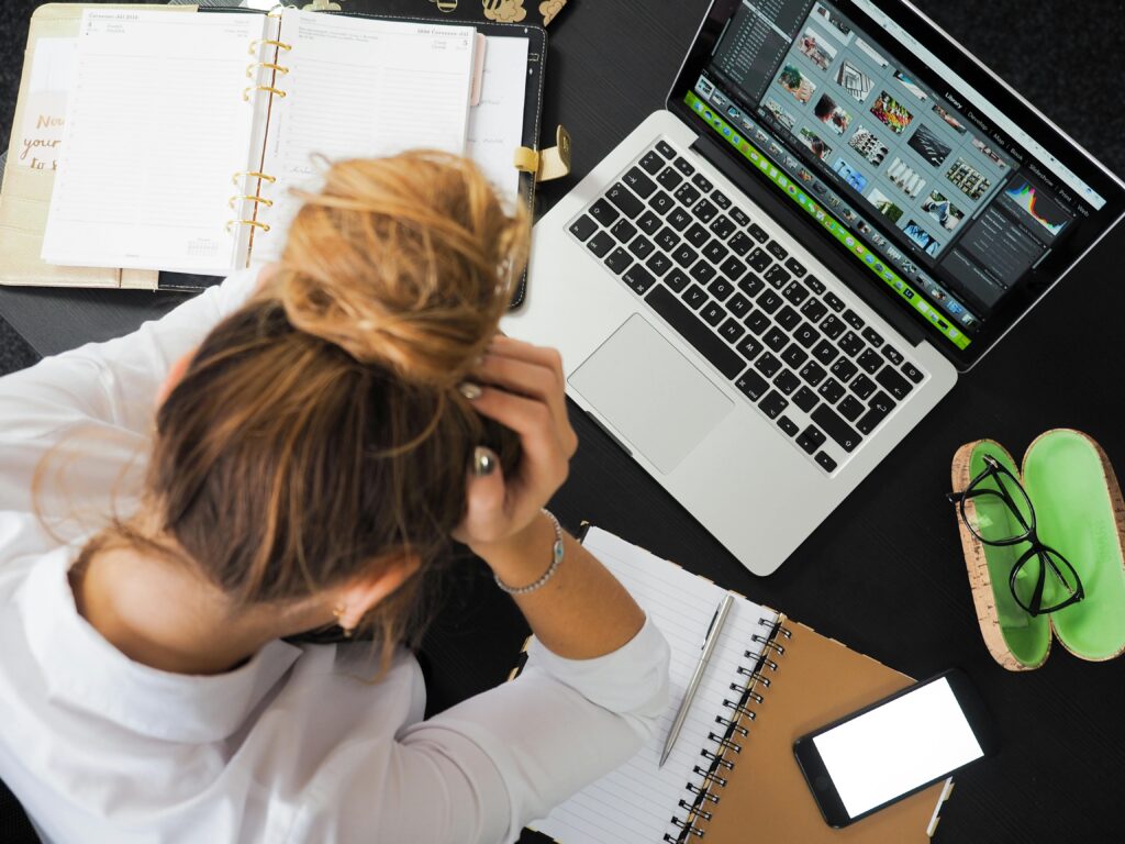 Vue aérienne d'une femme stressée travaillant à un bureau avec un ordinateur portable, un téléphone et des cahiers.