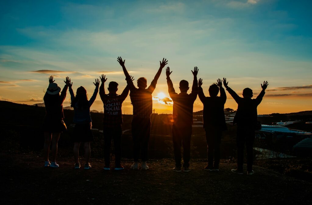Un groupe d'amis en contre-jour sur un couche de soleil lèvent les bras